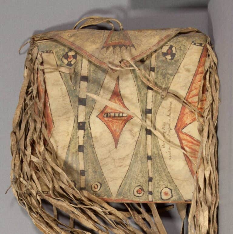 Plochá taška kmene Arapaho z 1. poloviny 19. století. Malována je červenou a zelenou barvou s černohnědou linkou. Tento exemplář je typickým příkladem staršího stylu malování surové kůže. Výrazné barvy přišly až mnohem později.