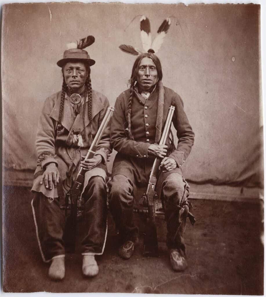 Hledač síly a Štíhlý muž, bojovníci kmene Atsina. Oba jsou vyzbrojeni opakovacími karabinami "yellow boy", Winchester 1866. Fotografie pochází z roku cca 1870. Autor Stanley Morrow.