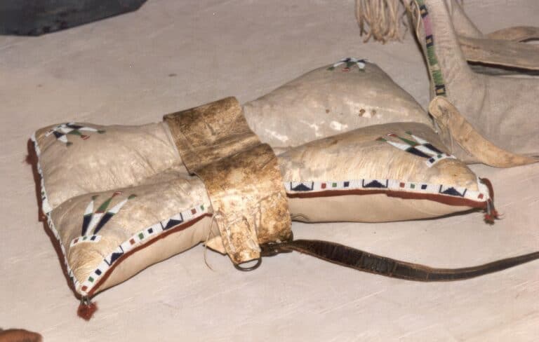 Polštářové sedlo kmene Lakotů z 2. poloviny 19. století. Zdobené je řadovým stehem korálek seed beads kolem obvodu a vyšívanými symboly orlích per v rozích