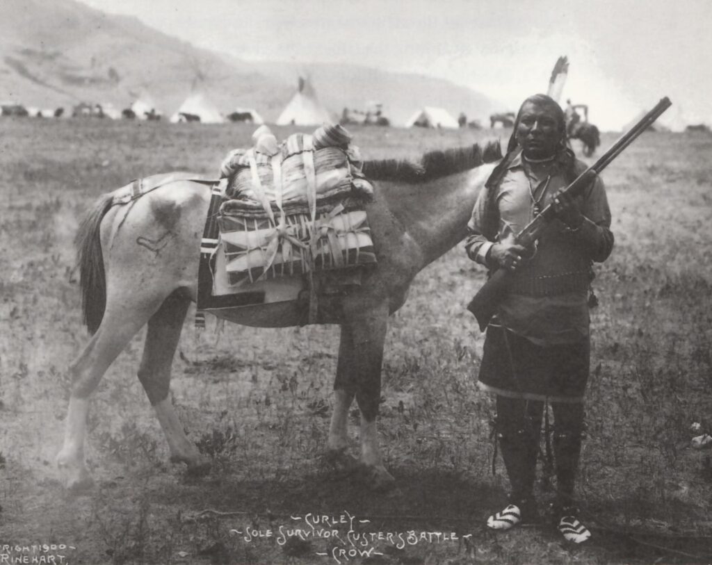 Curley, zvěd kmene Vran, který se jako mladík zúčastnil bitvy na Little Big Hornu. Ke svému nákladnímu sedlu má připevněn pár parfleší-obálek, každou na jedné straně sedla.