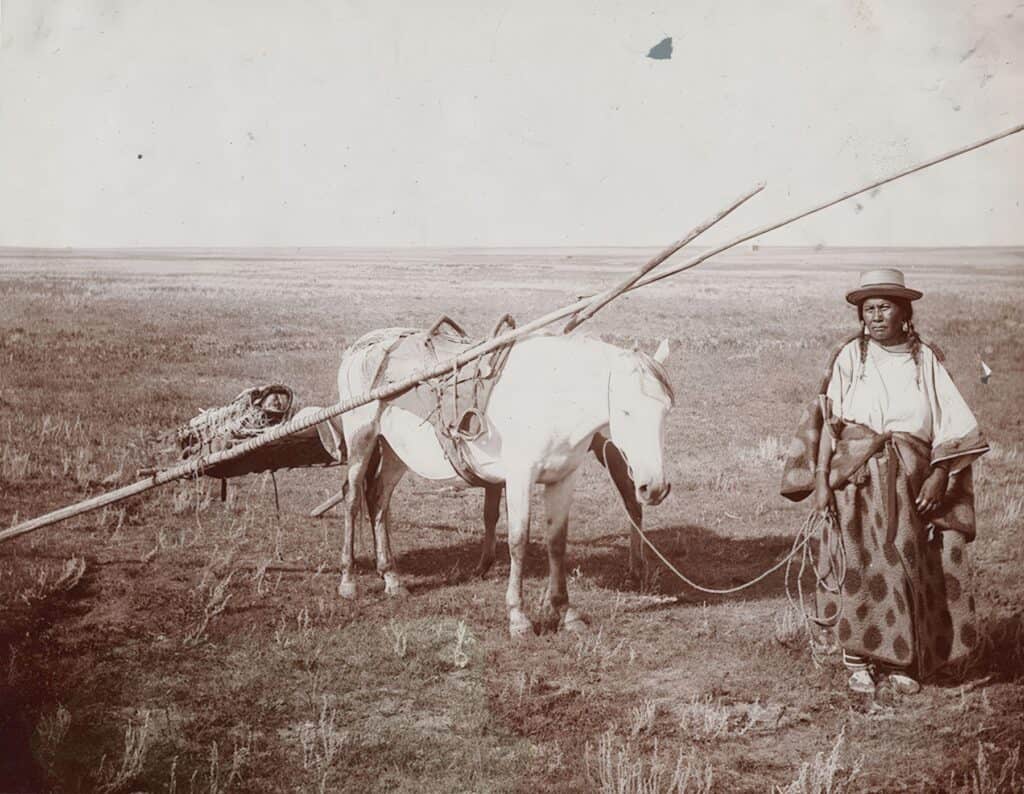 Žena ze severních plání na dobové fotografii. Její kůň má na sobě nákladní tetřívkové sedlo vypodložené bizoní kožešinou.