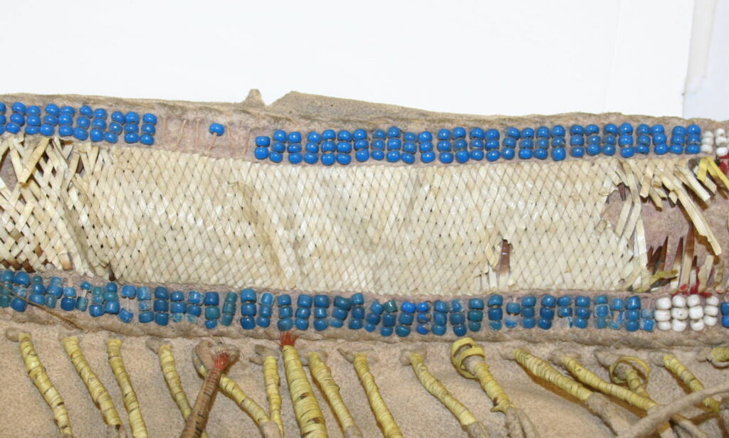 Pás válečné haleny kmene Vran. Je vyšit ursoními ostny a obšit korálky pound beads. British museum Londýn.