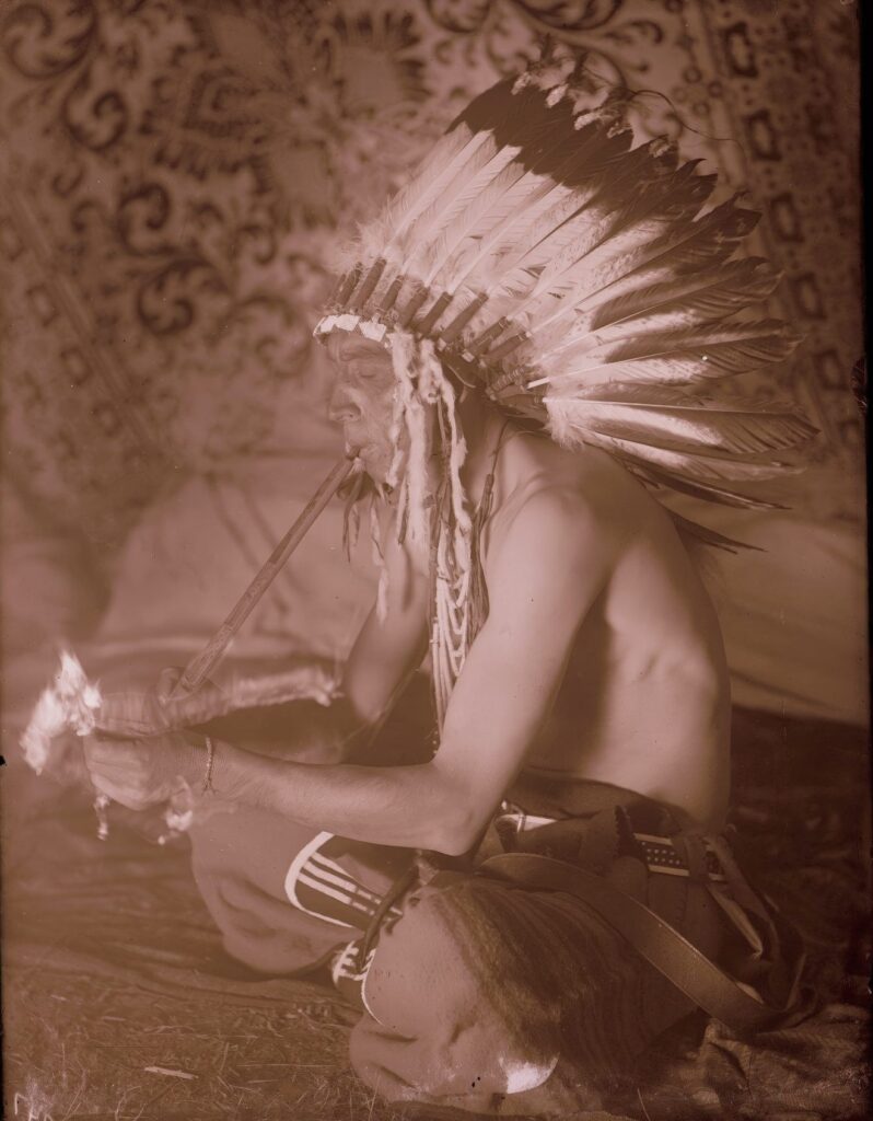 Válečník kmene Vran jménem "Krásný na kopci" kouří dýmku na dobové fotografii Richarda Throssela.