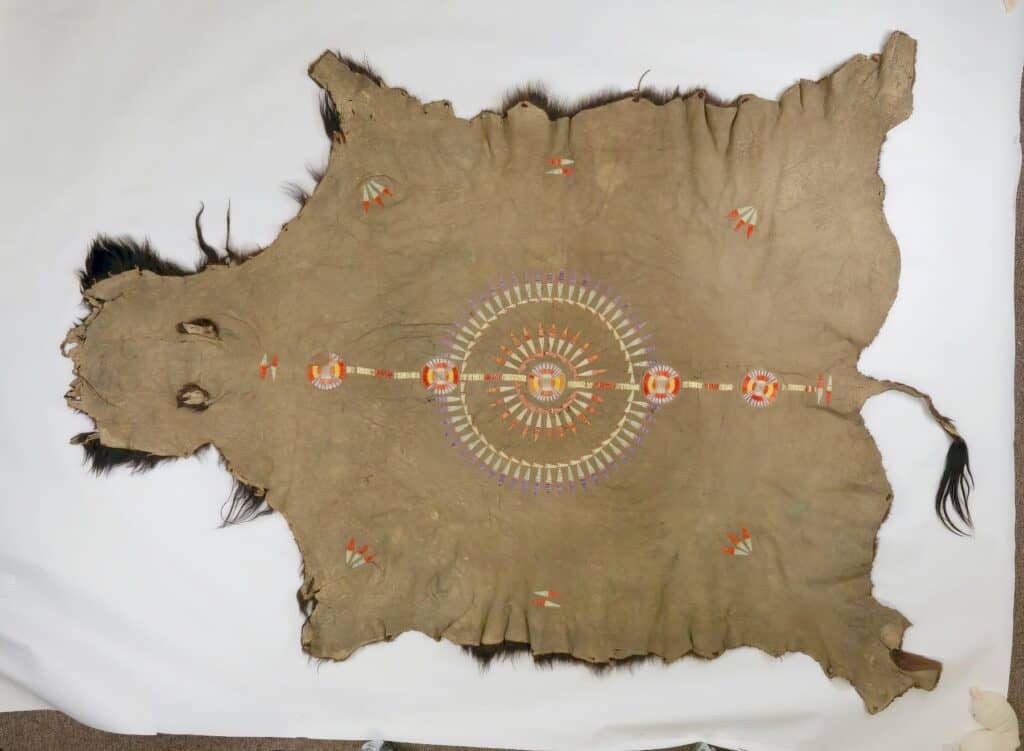 Bizoní plášť kmene Mandan. Ozdoben je quillovým pásem a symbolem slunce či péřové čelenky namalovanými hlinkou. Všimněte si typických švů. Pennsylvania museum.