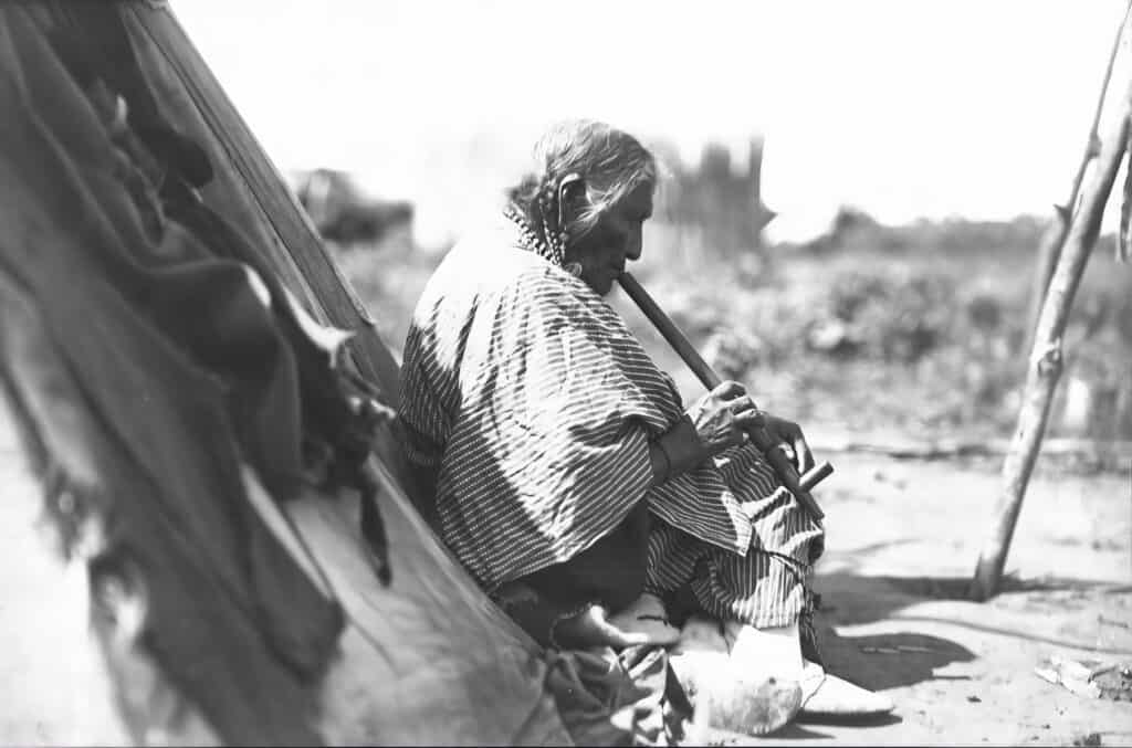 Stará žena Rudý korálek kouří dýmku. Fotografie George Grinnell.