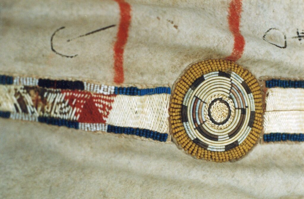 Detail bizoního plášťě s ozdobným pásem. Rozety jsou vyšity ostny na omotávaných žíních zatímco hranaté mezikusy jsou vyšity technikou proplétaného quillu. Bernisches historisches museum.