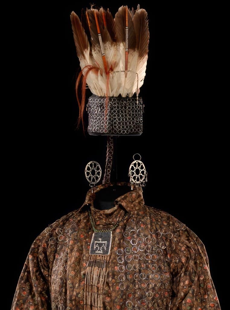 Čelenka a brokátová košile pokryté bezpočtem malých kruhových broží jsou součástí slavnostního obleku, který dostal britský důstojník Andrew Foster od Ojibwejů při slavnostní adopci za člena kmene před rokem 1790 v Michilimackinacu. Za pozornost stojí i kruhové náušnice.